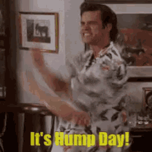 a man is dancing in a living room with the words `` it 's hump day '' written above him .