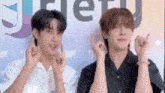 two young men are making hearts with their hands in front of a wall .