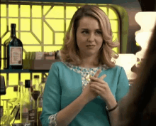 a woman in a blue top stands in front of a bar with bottles of alcohol