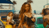 a woman in a bikini is standing in front of a group of women dancing in front of cars .