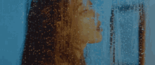 a woman stands in front of a window with rain drops falling on it