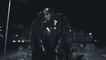 a woman with wings is walking down a street at night