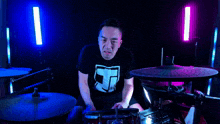 a man wearing a black shirt with the letter t on it plays drums
