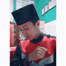 a young man wearing a black hat and a red and black jacket is sitting in a room .