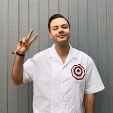 a man wearing a white shirt with a target on the front giving a peace sign