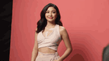 a woman is standing in front of a pink background wearing a crop top and skirt .