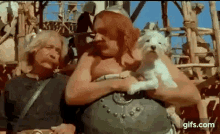 a man is holding a small white dog in his arms while sitting next to another man .