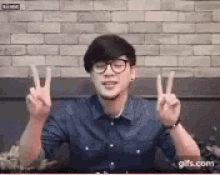 a young man wearing glasses and a blue shirt is giving a peace sign .