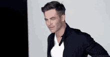 a man wearing a black jacket and a white t-shirt is winking at the camera .