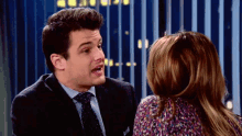 a man in a suit and tie is talking to a woman in a colorful shirt