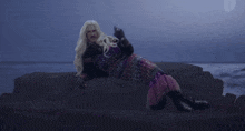 a woman in a mermaid costume is laying on a rock by the ocean