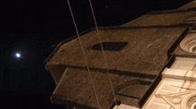 a building with a hole in the roof is lit up at night with a full moon in the background