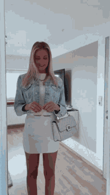a woman in a white dress and denim jacket holds a white purse