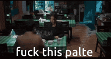 a man and a woman are sitting at a table in a restaurant with the words fuck this palte on the bottom