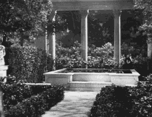 a black and white photo of a garden with columns and a fountain