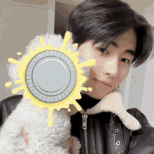 a man in a black jacket holds a small white dog in front of a yellow sun