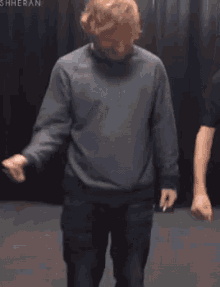 a man in a gray sweater is dancing in a room while holding a cigarette .