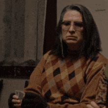 a woman wearing glasses and a plaid sweater holds a glass in her hand