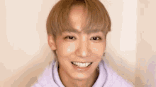 a young man with blonde hair is wearing a purple hoodie and smiling .