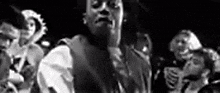 a black and white photo of a man in a suit standing in front of a crowd of people .