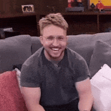a man with glasses is smiling while sitting on a grey couch