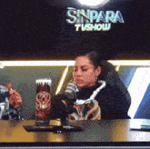 a woman sits in front of a sinpara tv show sign
