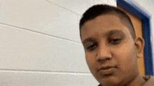 a young boy with short hair is standing in front of a white brick wall and a blue door .