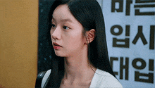 a young woman with long black hair is standing in front of a sign that says ' a ' on it .