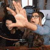 a woman wearing glasses and headphones is reaching out her hand in front of a microphone