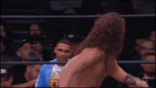 a man in a blue jacket is watching a wrestler in a ring with aew written on the bottom
