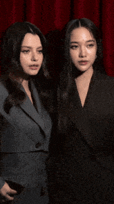 two women are standing next to each other wearing suits and looking at the camera