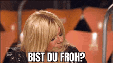 a woman with blonde hair is sitting in a chair with the words bist du froh written on her face .