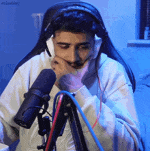a man wearing headphones and a headset is sitting in front of a microphone with his hand on his chin .