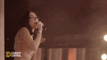 a woman singing into a microphone with comedy central on the bottom right