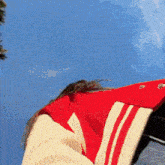 a woman wearing a red and white varsity jacket is looking up at the sky