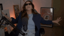 a woman wearing sunglasses is standing in front of a microphone with her arms outstretched