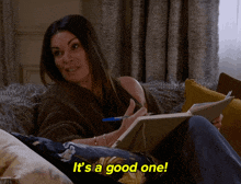a woman sits on a couch holding a notebook and a pen and the words it 's a good one