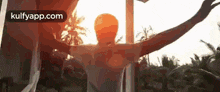 a man is standing in a hammock with his arms outstretched in front of a sunset .