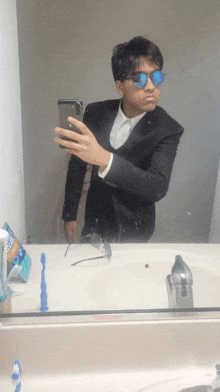 a man in a suit and sunglasses is taking a selfie in a bathroom mirror