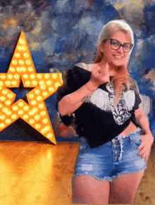 a woman wearing shorts and glasses stands in front of a star with lights on it