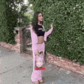 a woman in a pink outfit is standing next to a bush