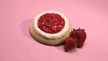 two strawberries are sitting on top of a cake with whipped cream on a pink surface .