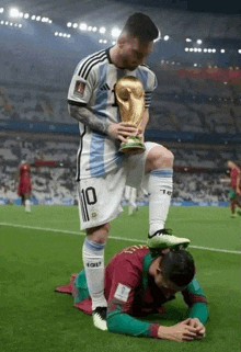 a soccer player kneeling on another soccer player 's knee while holding a trophy .