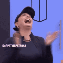 a woman wearing a baseball cap is laughing and clapping her hands .