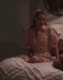 a woman in a yellow dress sits on a bed with her legs crossed