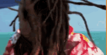 a woman with dreadlocks is wearing a hawaiian shirt and looking at the camera .
