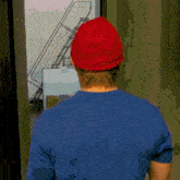 a man wearing a red hat and a blue shirt is looking out a window