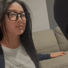 a woman wearing glasses is sitting on a couch and looking at the camera .