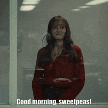 a woman in a red shirt is standing in front of a window and says good morning sweetpeas
