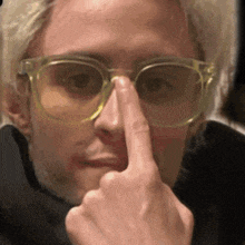 a man wearing glasses is touching his nose with his index finger